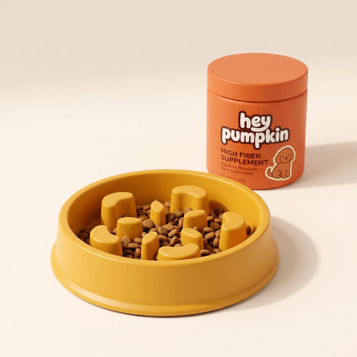 The Slow Bowl, a yellow slow feeder dog bowl with moulded ridges holding dry food, next to a tub of Hey Pumpkin high fiber supplement